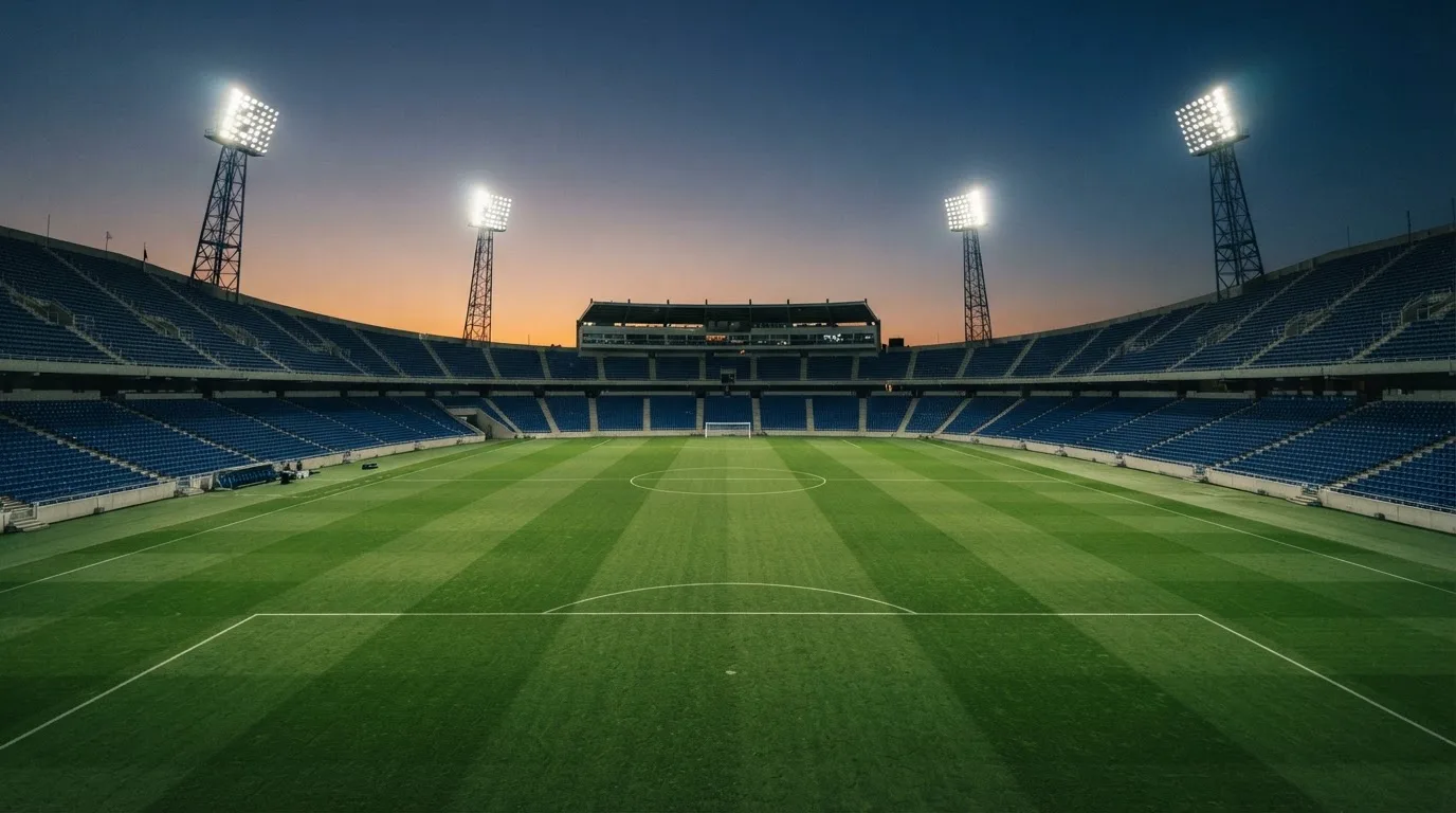 Een leeg voetbalstadion met lichtmasten bij schemering