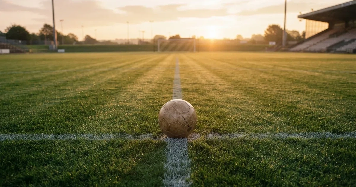 Een voetbal op de middenstip van een grasveld in het ochtendlicht