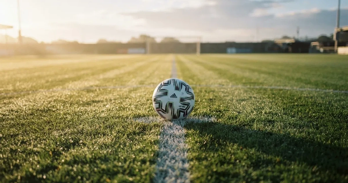 Een voetbal op de middenstip van een grasveld in het ochtendlicht