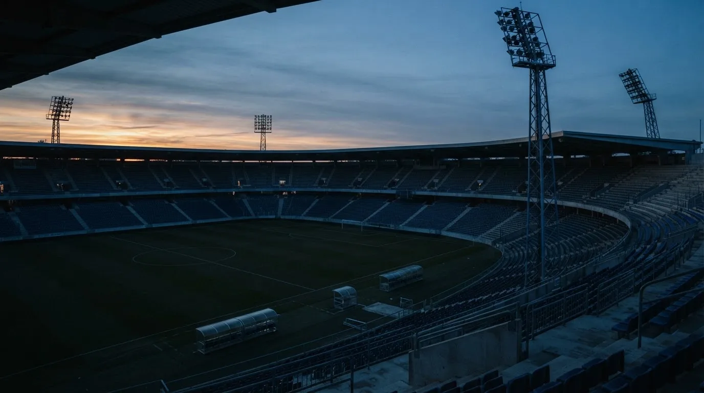 Een leeg voetbalstadion met lichtmasten bij schemering