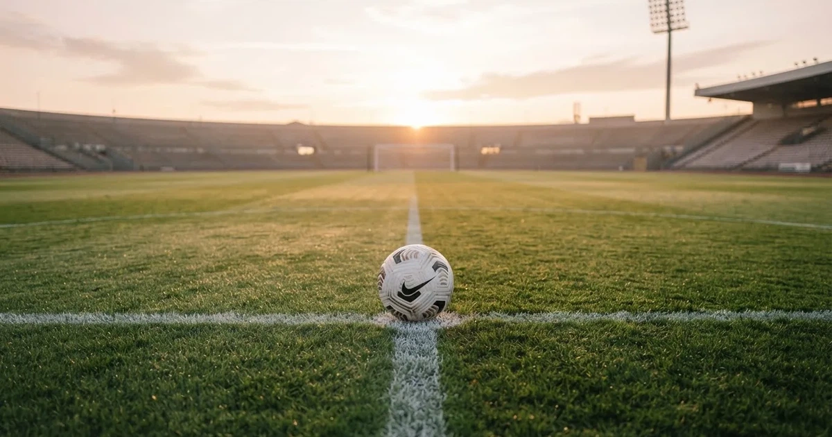 Een voetbal op de middenstip van een grasveld in het ochtendlicht