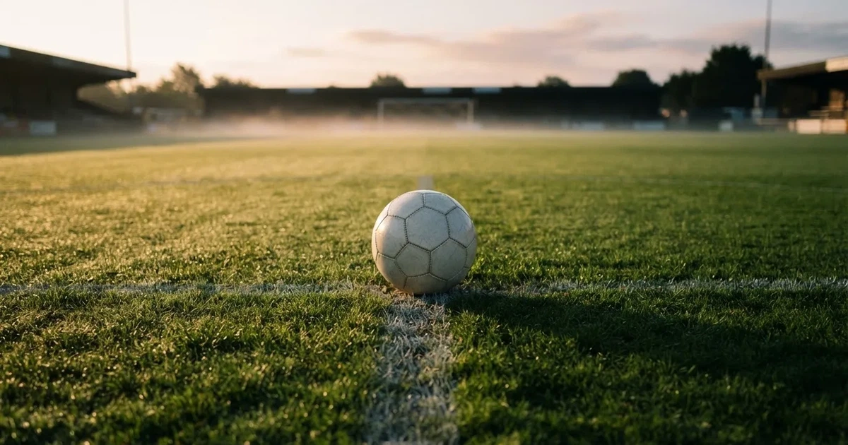 Een voetbal op de middenstip van een grasveld in het ochtendlicht