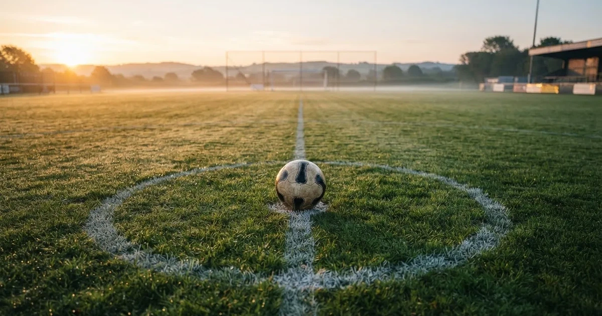 Een voetbal op de middenstip van een grasveld in het ochtendlicht